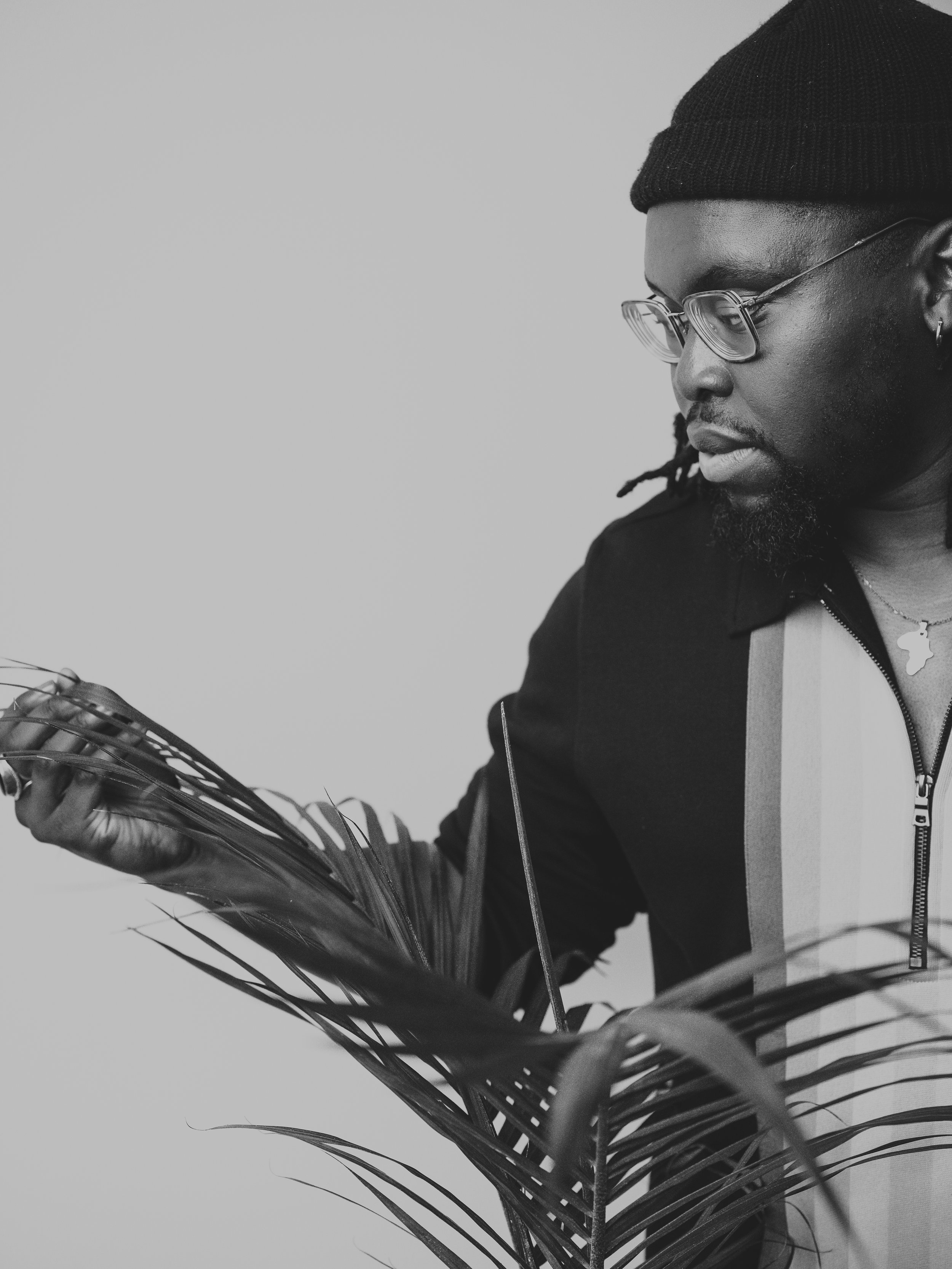 A man with a beanie and glasses poses with a plant